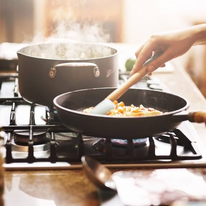 kuhar za štednjakom kuha u tavi i loncu