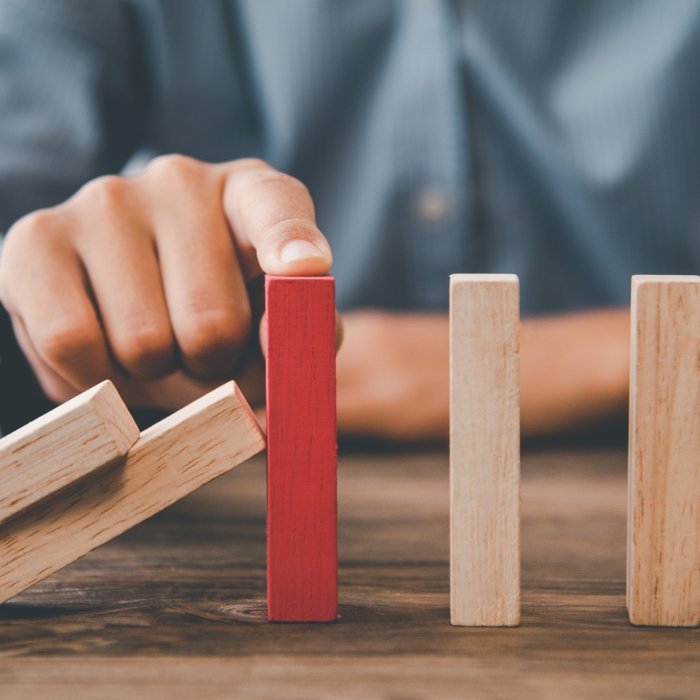 Muška ruka u odijelu zaustavlja efekt domina kod štapića obojanog u crveno.