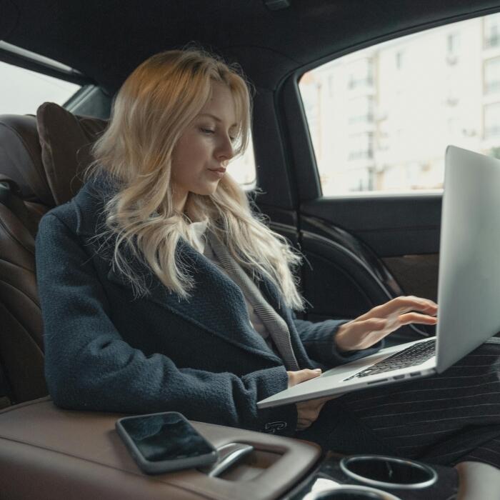 poslovna žena u sivom odijelu radi na računalu na zadnjem sjedištu automobila
