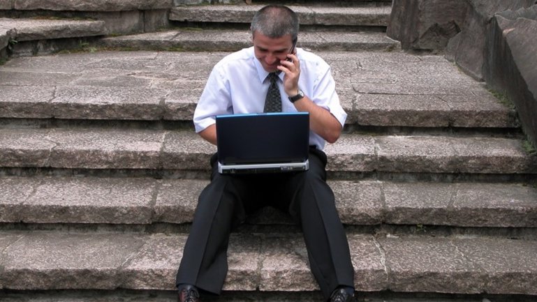 Gospodin sjedi na stepenicama i radi na laptopu