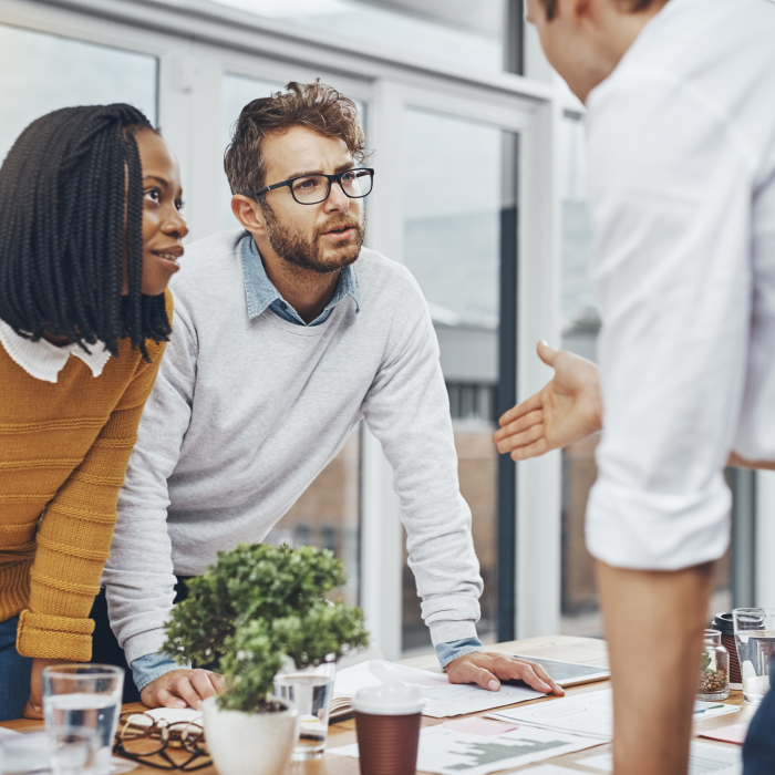 Dva muškarca i žena raspravljaju za uredskim stolom stojeći.
