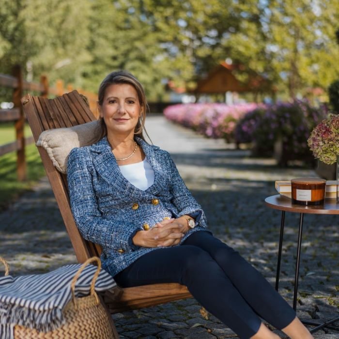 Tanja sjedi na drvenoj stolici u prirodi u plavom sakou s osmijehom na licu