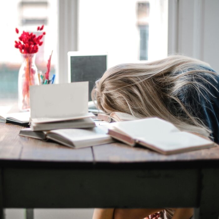 Mlada žena zaspala za stolom punim knjiga i računalom